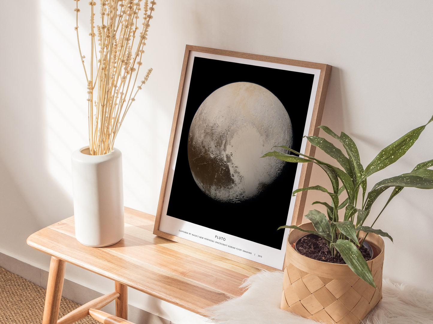 Framed Pluto print on a wooden side table with plants and a vase.