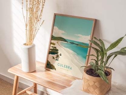 A framed poster of Culebra, Puerto Rico, rests on a wooden bench beside a white vase with dried stems and a potted green plant. Sunlight casts shadows on the wall.