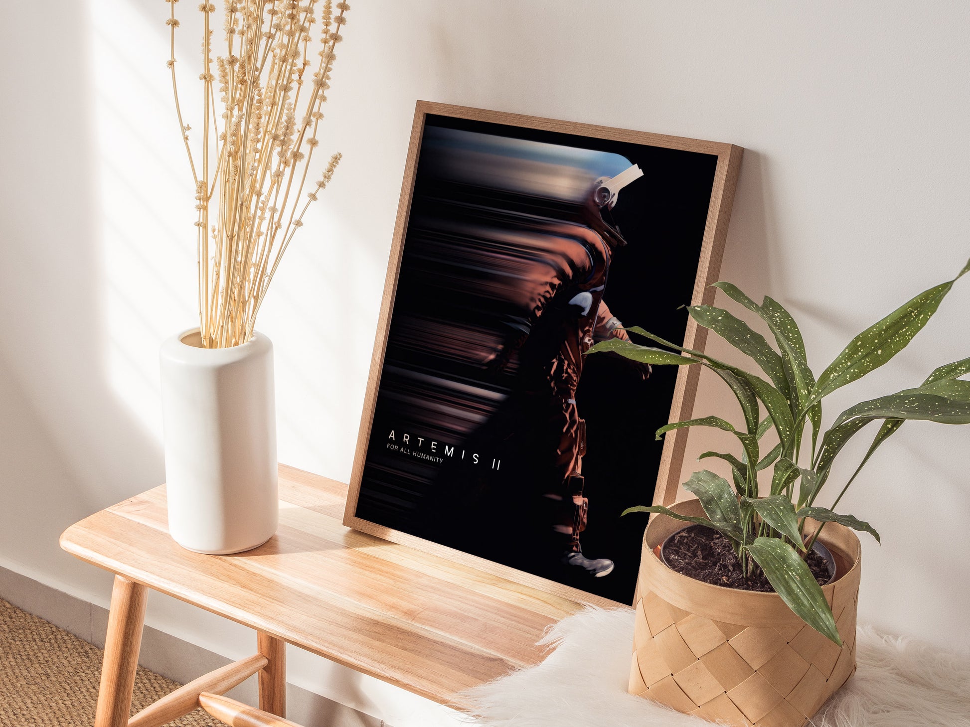 Natural wood framed Artemis II space print leaning on a shelf next to plants and neutral accessories