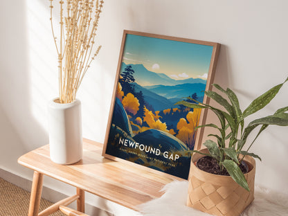 A framed Newfound Gap poster depicting blue-hued mountains and a sunlit sky rests on a wooden bench. It is surrounded by a white vase with dried stems and a potted green plant in a woven basket. Sunlight filters through a nearby window.