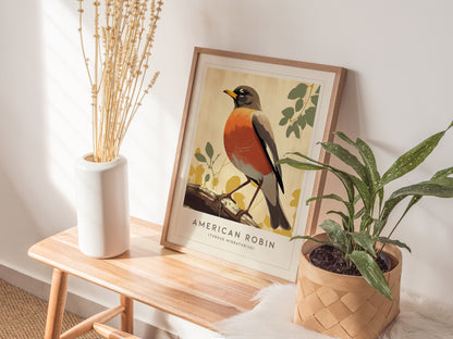 A framed American Robin poster sits on a wooden bench, flanked by a white vase with dried flowers and a potted plant. Sunlight casts soft shadows.