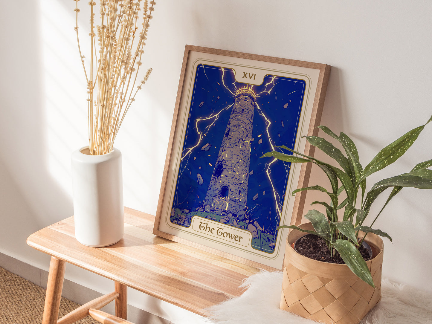 A framed poster of The Tower tarot card is displayed on a wooden table, featuring a tall, stone tower struck by lightning, surrounded by falling figures.