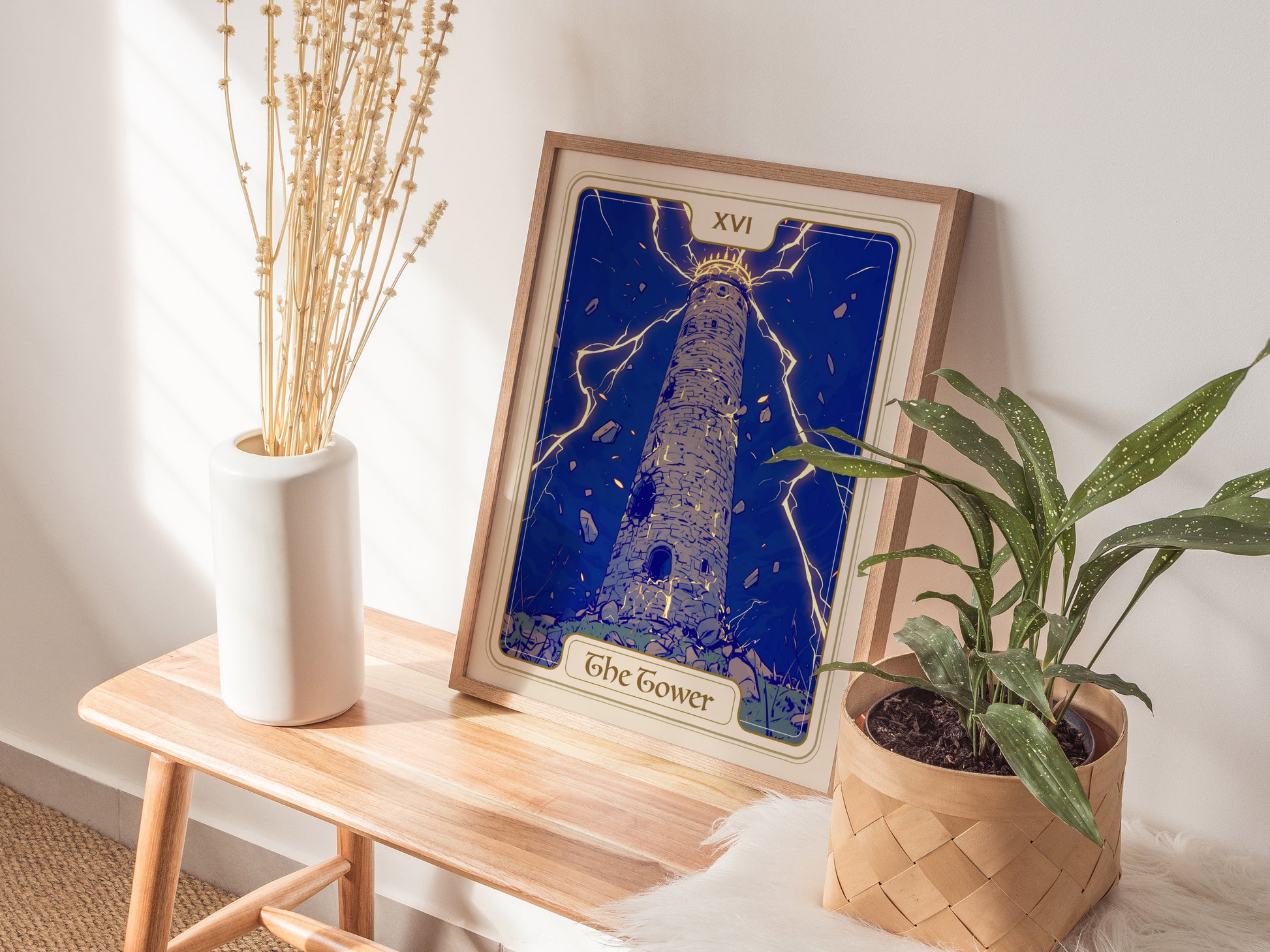 A framed poster of The Tower tarot card is displayed on a wooden table, featuring a tall, stone tower struck by lightning, surrounded by falling figures.