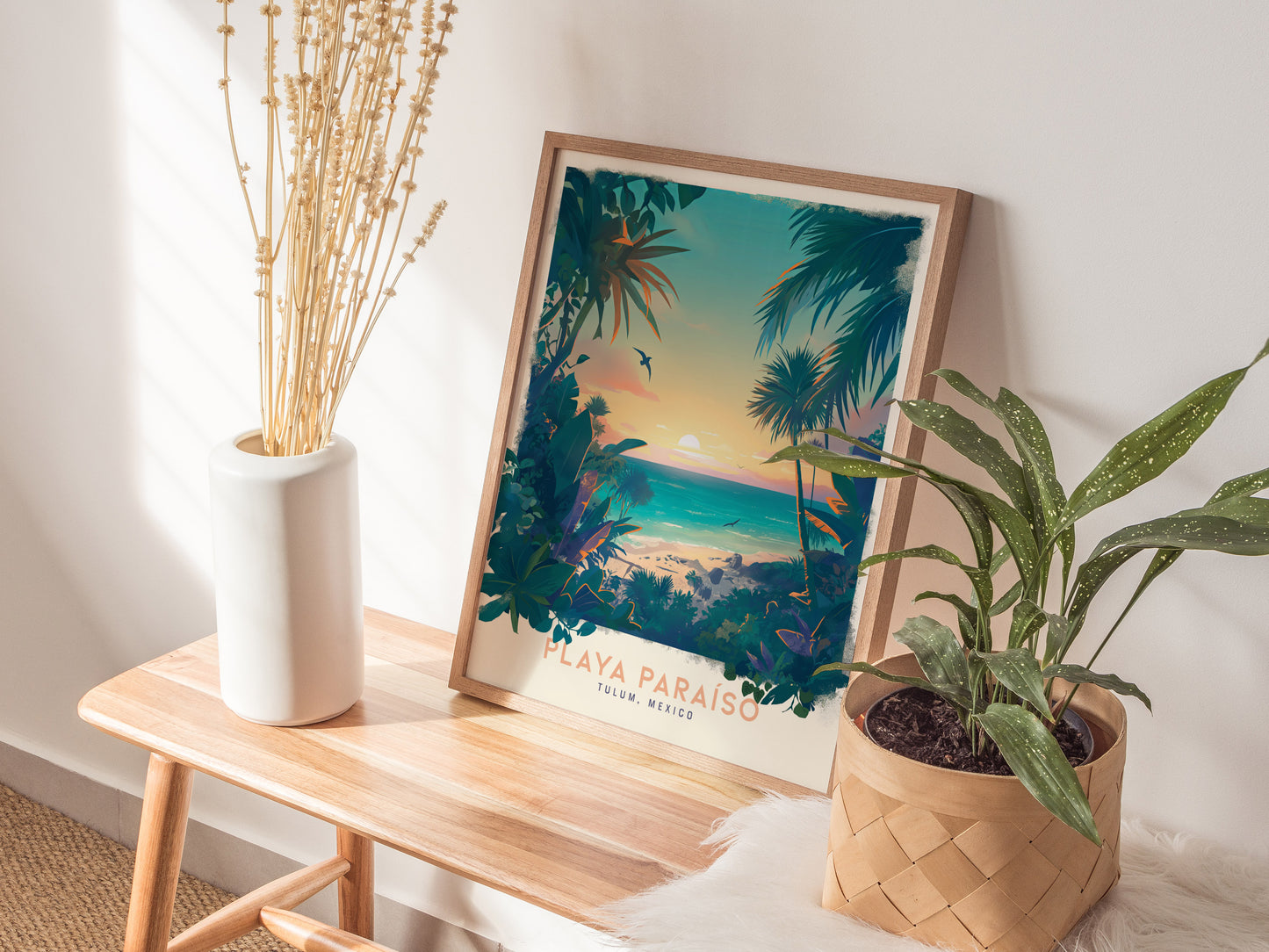 A framed Playa Paraiso poster depicting a tropical beach scene is placed on a wooden bench, accompanied by a white vase with dried flowers and a potted plant.
