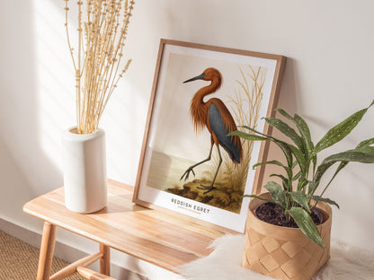 A framed poster featuring a reddish egret is propped on a wooden bench, accompanied by a white vase with dried stems and a potted plant. The wall art adds a natural touch to the cozy setting.