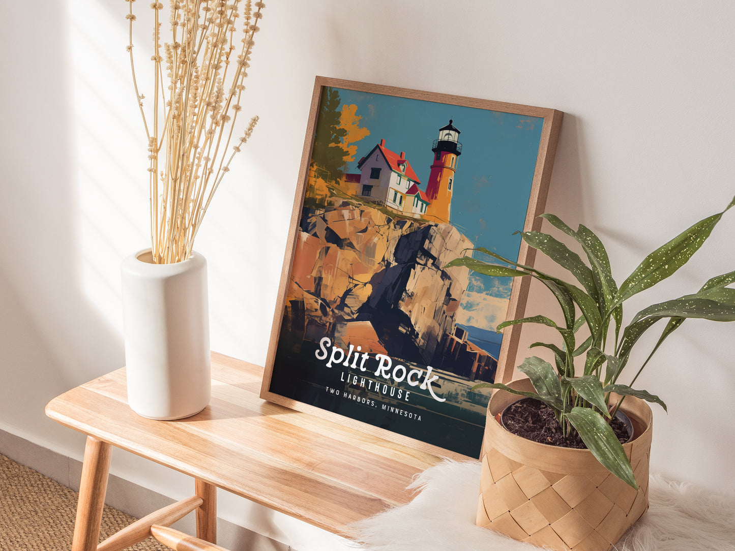A framed Split Rock Lighthouse poster rests on a wooden bench, accompanied by a white vase with dried flowers and a potted green plant.