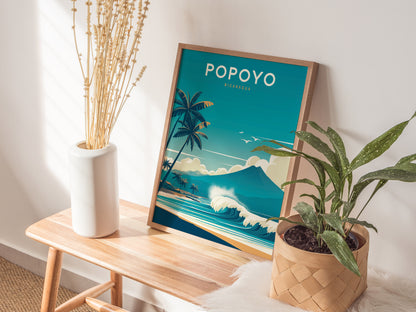 A framed Popoyo Nicaragua poster featuring waves and palm trees is placed on a wooden bench next to a white vase with dried flowers and a potted green plant.