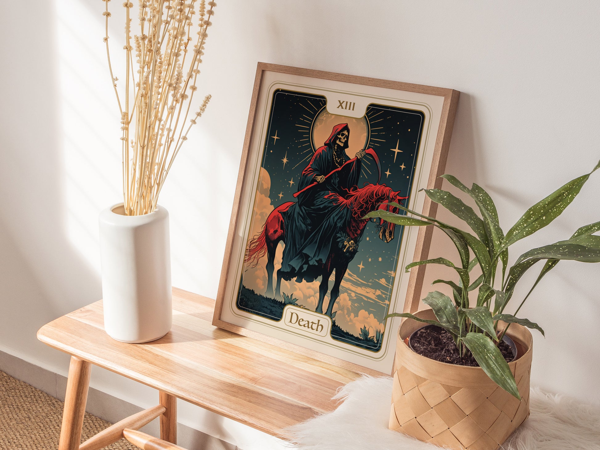 A framed Death Major Arcana tarot card poster featuring a skeletal rider on horseback is displayed on a wooden bench, surrounded by a white vase with dried flowers and a.