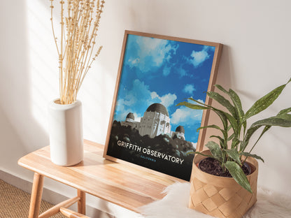 A framed Griffith Observatory poster leans against a wall on a wooden bench, flanked by a white vase with dried flowers and a potted green plant.