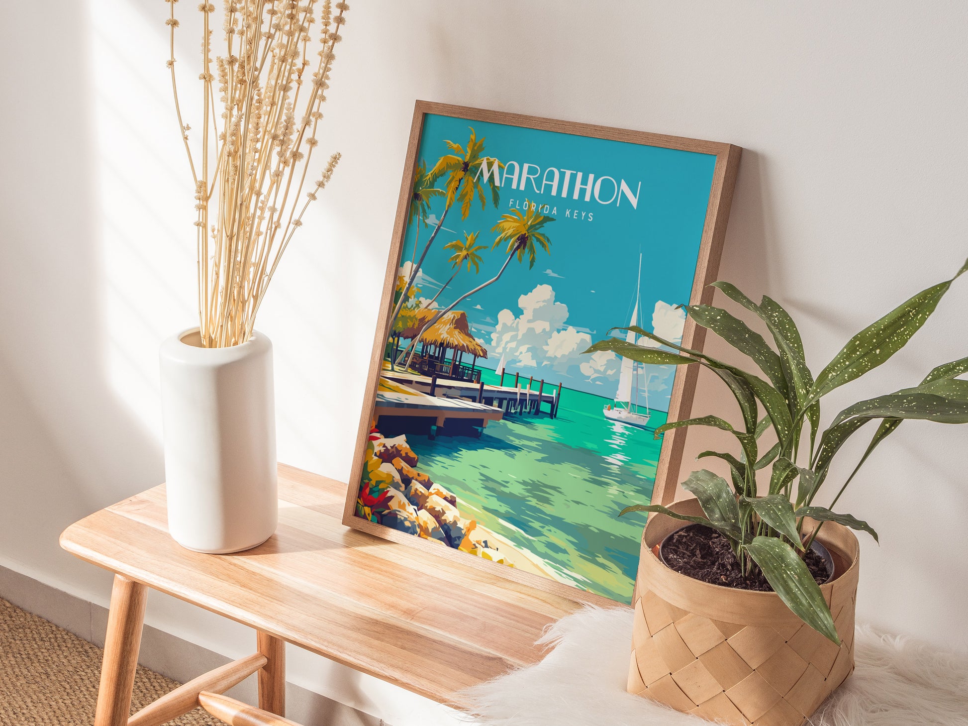 A framed Marathon Florida Keys poster featuring a tropical beach scene with palm trees and turquoise water sits on a wooden table beside a white vase and a potted plant.