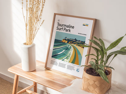 A framed Tourmaline Surf Park poster sits on a wooden bench between a white vase with dried flowers and a potted plant. Sunlight casts shadows on the wall.