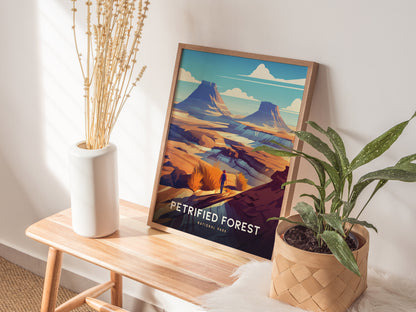 A framed Petrified Forest National Park poster rests on a wooden bench, flanked by a white vase with dried plants and a potted green plant in a woven basket.
