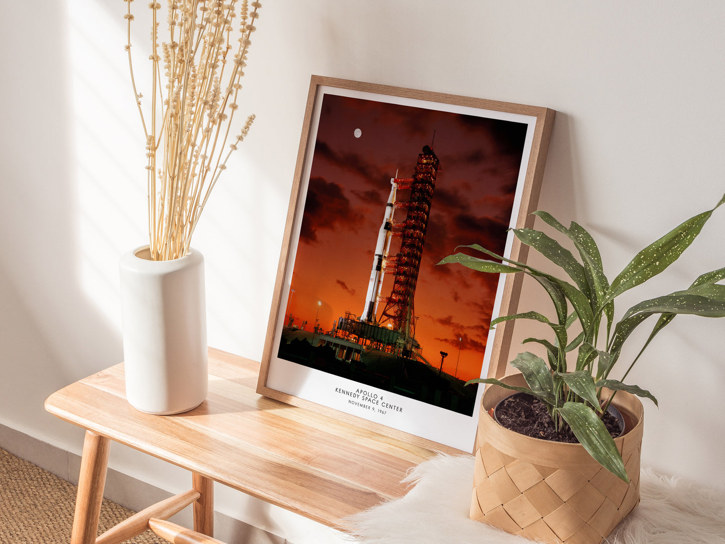 Natural wood framed Apollo 4 Saturn V rocket print leaning on a shelf next to plants and neutral accessories