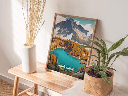 A framed Wing Lake Washington poster rests on a wooden bench, flanked by a white vase with dried flowers and a potted plant, in a sunlit room.