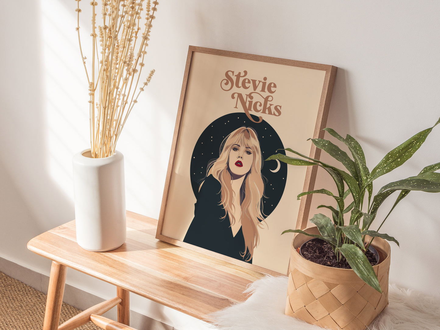 A framed poster featuring an illustrated portrait of a woman with long blonde hair, set against a starry black background, is displayed on a wooden bench beside plants.
