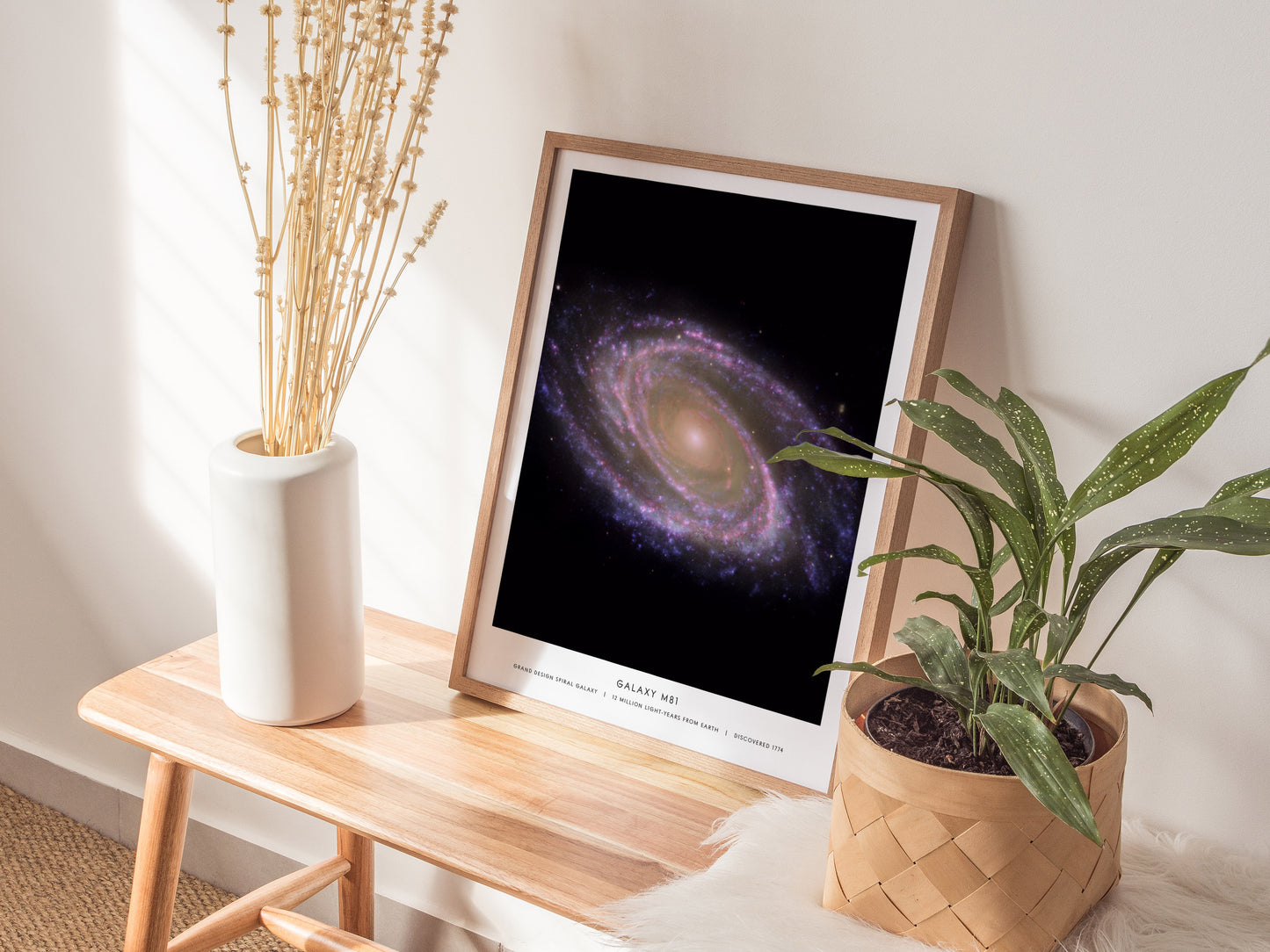Natural wood framed M81 space print leaning on a shelf with plants and neutral accessories