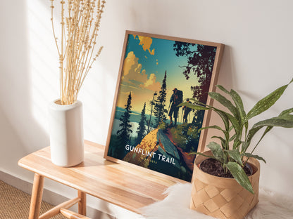 A framed Gunflint Trail poster featuring hikers and pine trees is displayed on a wooden bench, accompanied by a white vase with dried stems and a potted plant.