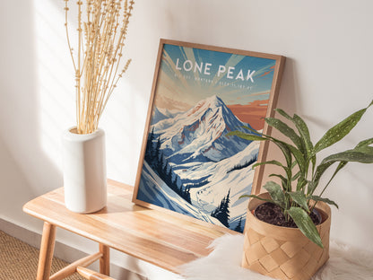 A framed Lone Peak Big Sky poster rests on a wooden bench beside a white vase of dried flowers and a potted green plant, with sunlight casting shadows.