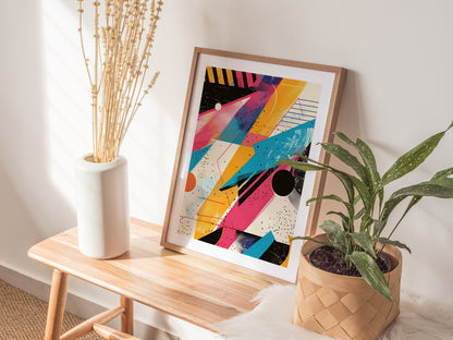 A vibrant 1980s-style abstract poster with geometric patterns is framed and placed on a wooden bench. It is flanked by a white vase with dried plants and a potted green.
