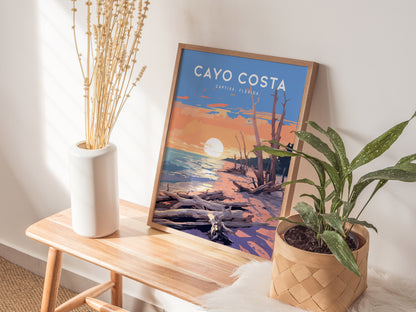 A framed poster of Cayo Costa, Captiva, Florida, featuring a sunset over driftwood and water, rests on a wooden bench beside a white vase and potted plant.