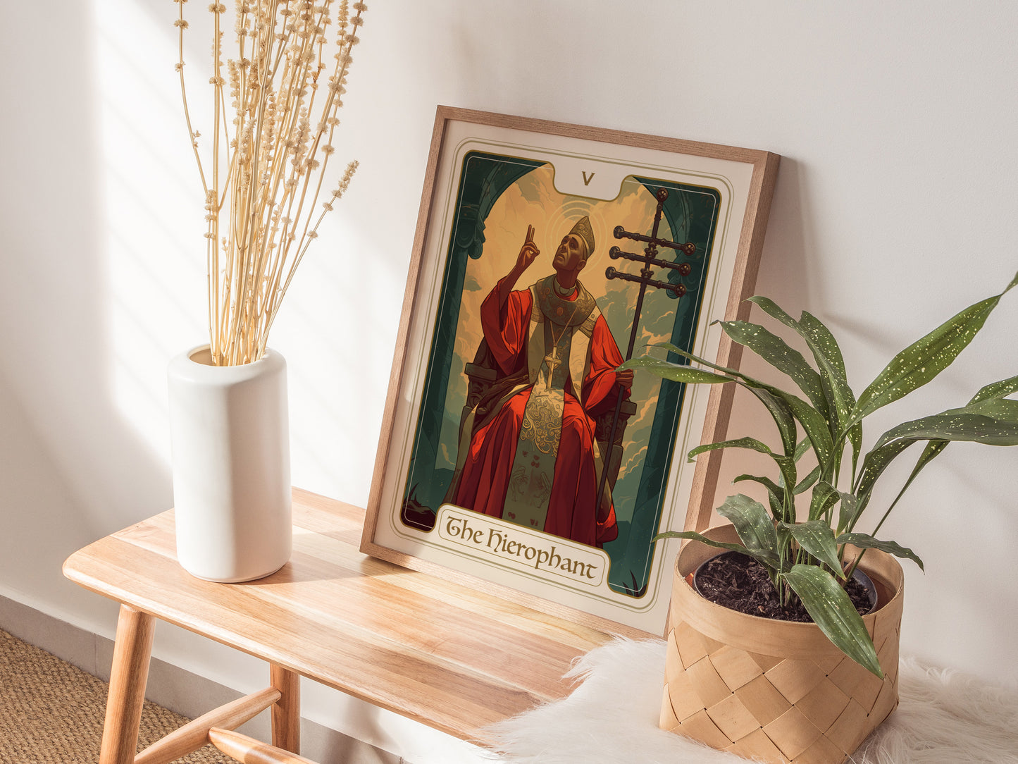 A Hierophant Tarot Card poster rests on a wooden bench alongside a white vase with dried flowers and a potted green plant, creating a serene decor setting.