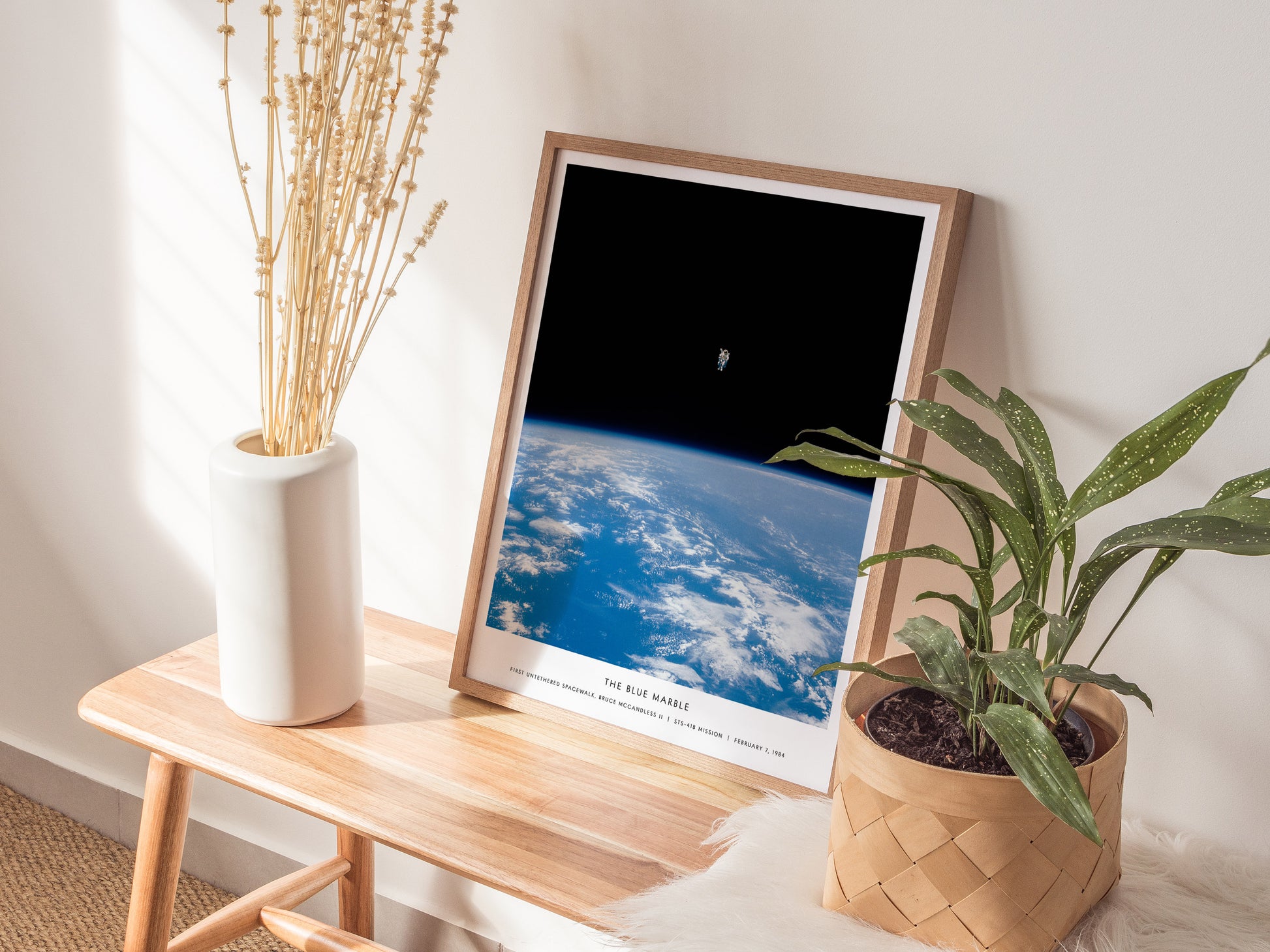 Natural wood framed Blue Marble NASA spacewalk print leaning on a shelf next to plants and neutral accessories