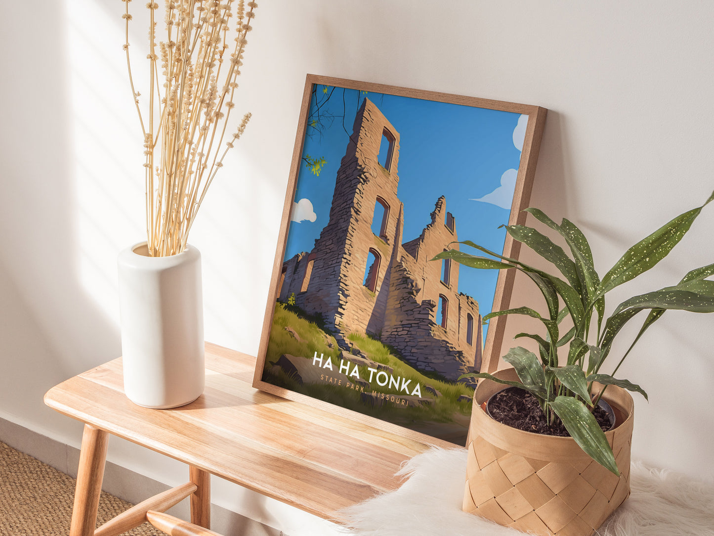 A framed Ha Ha Tonka State Park poster with castle ruins is displayed on a wooden bench, accompanied by a white vase with dried flowers and a potted plant.