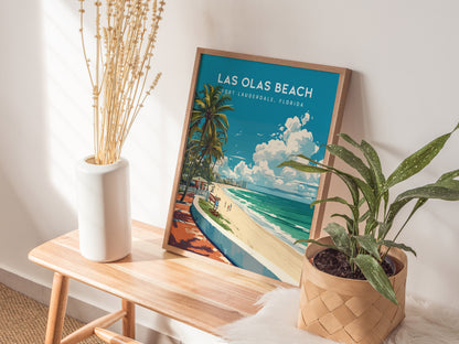 A Las Olas Beach poster featuring palm trees and a beach scene is propped against a wall, beside a white vase with dried branches and a potted plant.