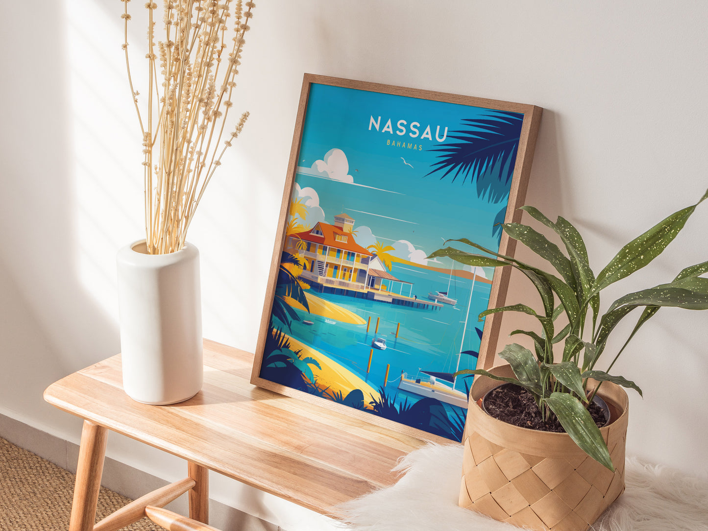 A Nassau Bahamas poster with vibrant colors leans against a wall on a wooden bench. Nearby, a white vase with dried stems.