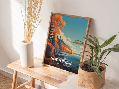 A framed poster titled North Shore, Lake Superior, Minnesota is displayed on a wooden table. The artwork features vibrant autumn foliage along rocky shores, with a tranquil lake and a clear blue sky, complemented by a decorative plant.