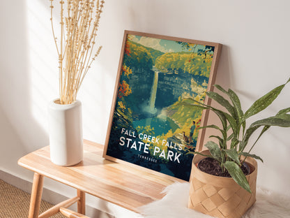 A framed Fall Creek Falls State Park poster rests on a wooden bench beside a white vase with dried plants and a potted green plant, creating a cozy decor setting.