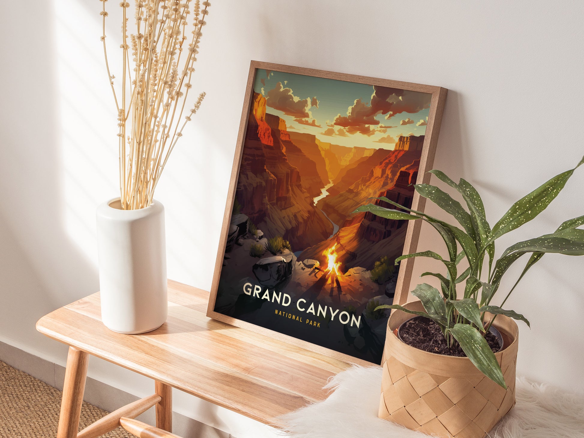 A framed Grand Canyon poster is displayed on a wooden bench beside a white vase with dried flowers and a potted green plant.