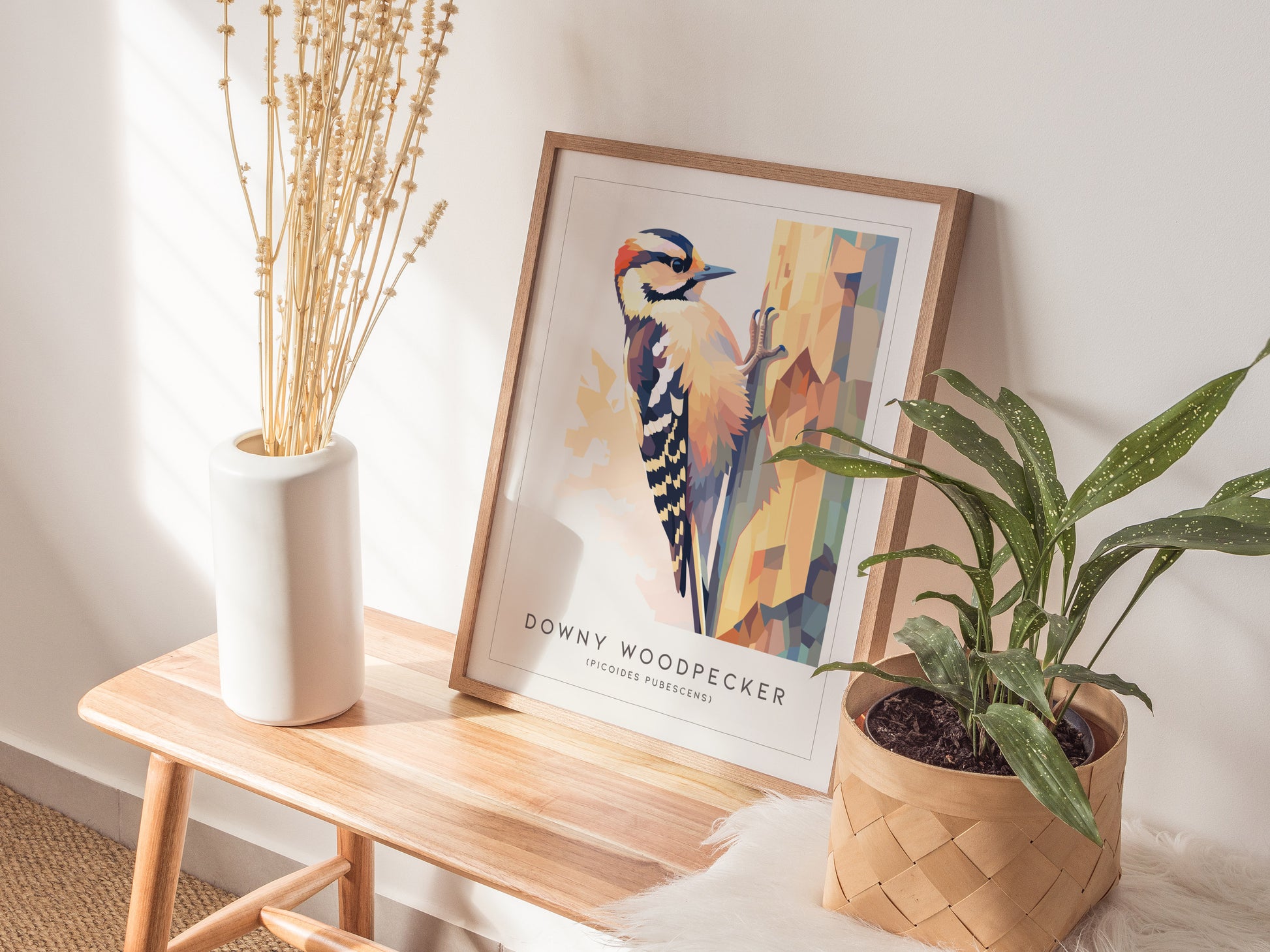 Framed abstract art print of a Downy Woodpecker in geometric low-poly style, featuring warm pastels on a tree trunk. Perfect wildlife art for nature lovers.