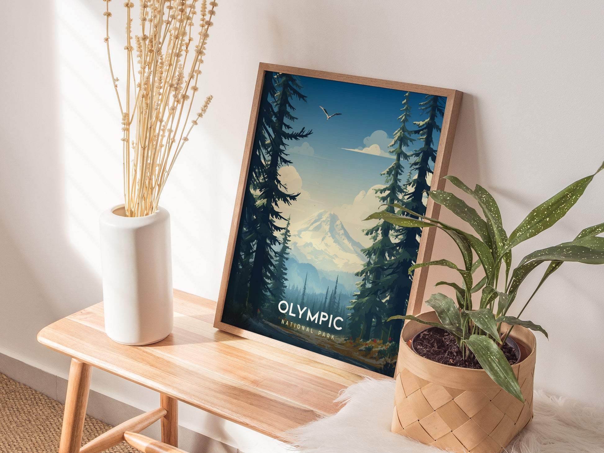 Framed Olympic National Park poster with a mountain and forest scene sits on a wooden bench, next to a potted plant and a vase of dried flowers.