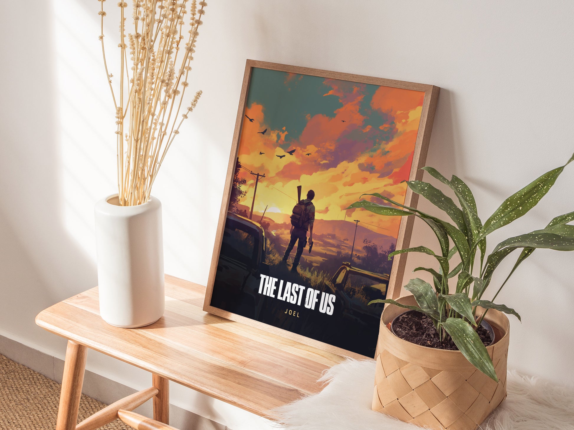 A framed The Last of Us poster featuring a silhouette of a person against a vibrant sunset is placed on a wooden bench next to a white vase and a.