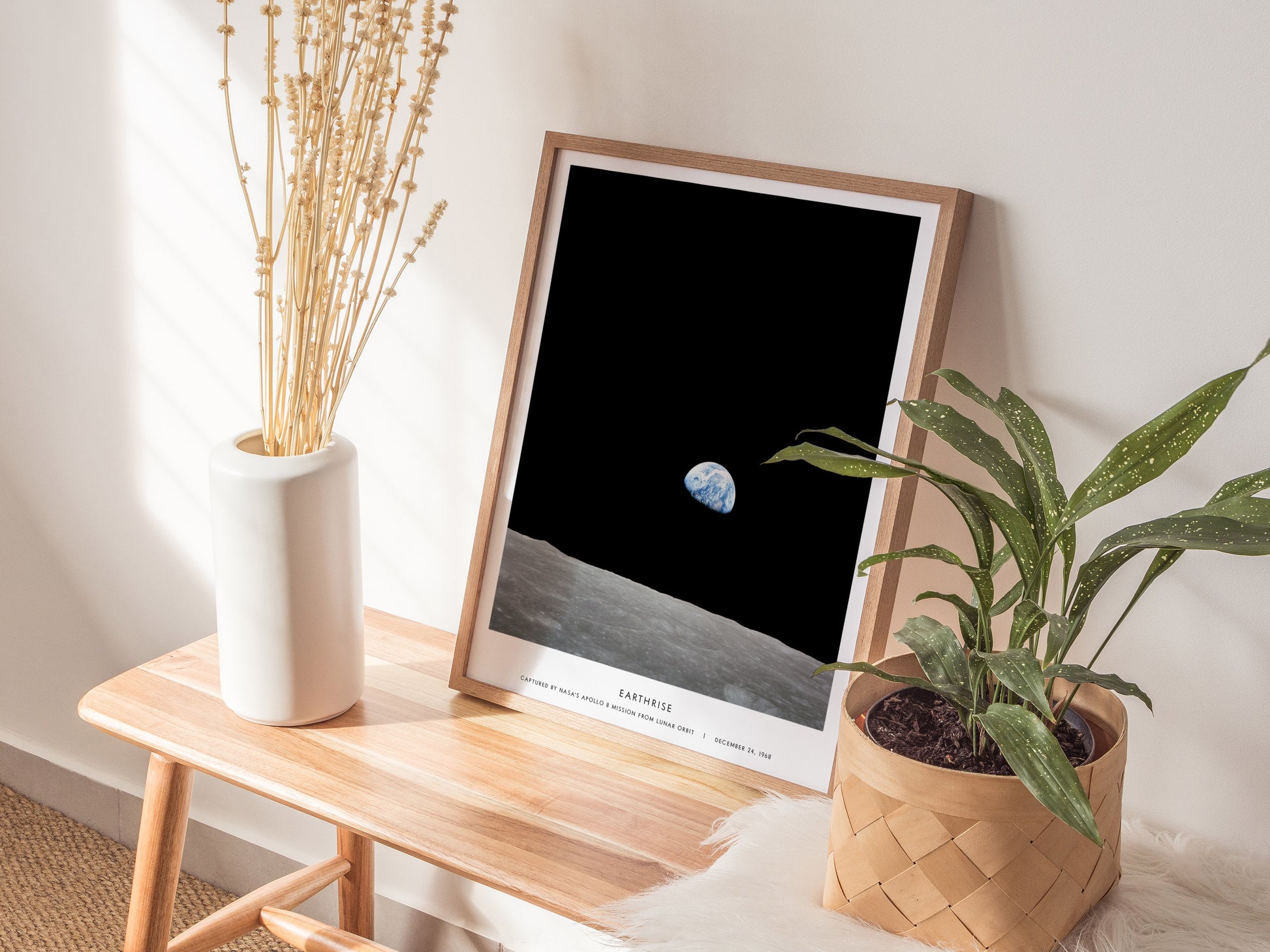 Natural wood framed Earthrise space print leaning on a shelf next to plants and neutral accessories