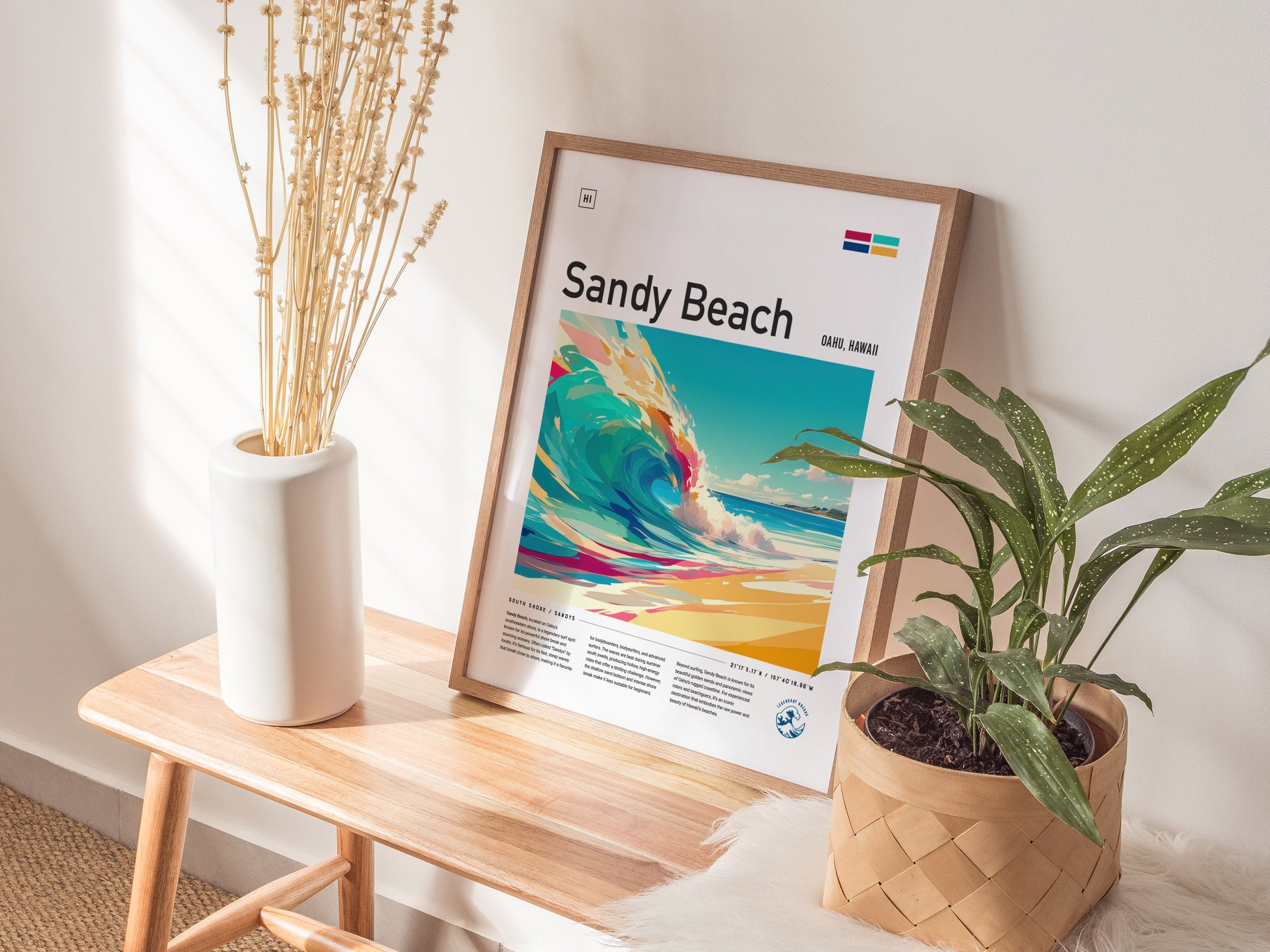 A framed Sandy Beach poster featuring a colorful wave is displayed on a wooden bench, alongside a white vase with dried branches and a potted plant.