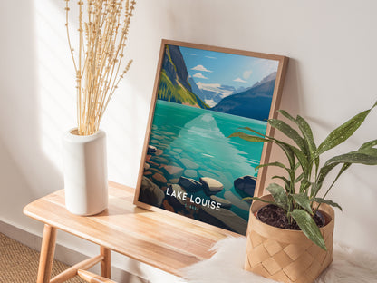 A framed Lake Louise poster rests on a wooden bench beside a white vase with dried flowers and a potted green plant, creating a serene, natural decor setting.