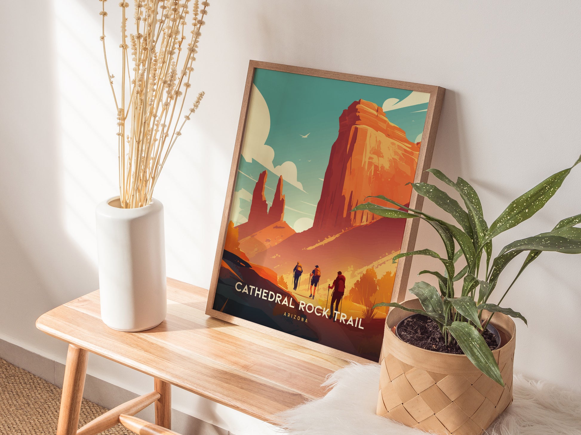 A framed Cathedral Rock Trail poster rests on a wooden bench beside a white vase with dried flowers and a potted green plant, creating a serene, natural atmosphere.