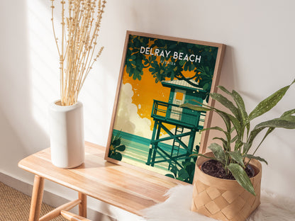 A Delray Beach poster with a vibrant orange and green design featuring a lifeguard stand leans against a wall on a wooden bench, alongside a potted plant and a white.