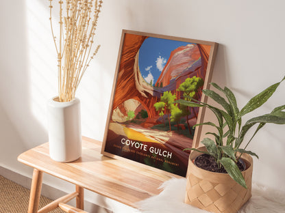 A framed Coyote Gulch poster leans against a wall on a wooden bench, surrounded by a white vase with dried flowers and a potted plant.