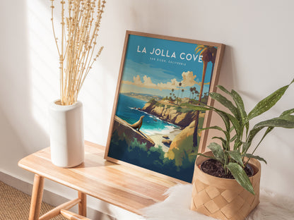 A framed poster of La Jolla Cove, featuring coastal cliffs and palm trees, is displayed on a wooden bench with a white vase and a potted plant nearby.
