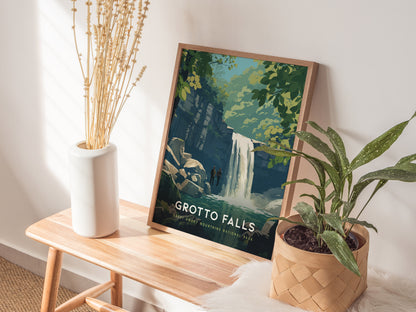 A framed Grotto Falls poster is displayed on a wooden bench beside a white vase with dried flowers and a potted green plant. The poster features a waterfall scene with lush greenery, creating a serene and natural setting.