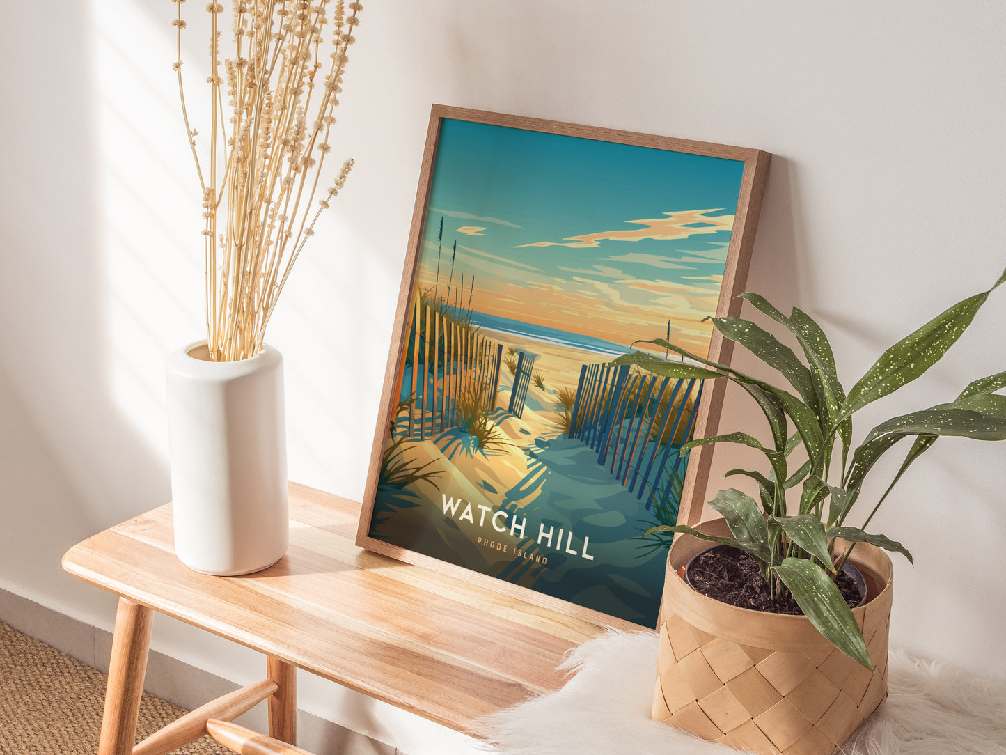 A framed Watch Hill Rhode Island poster depicting a coastal scene is propped on a wooden bench, flanked by a white vase with dried flowers and a potted plant.