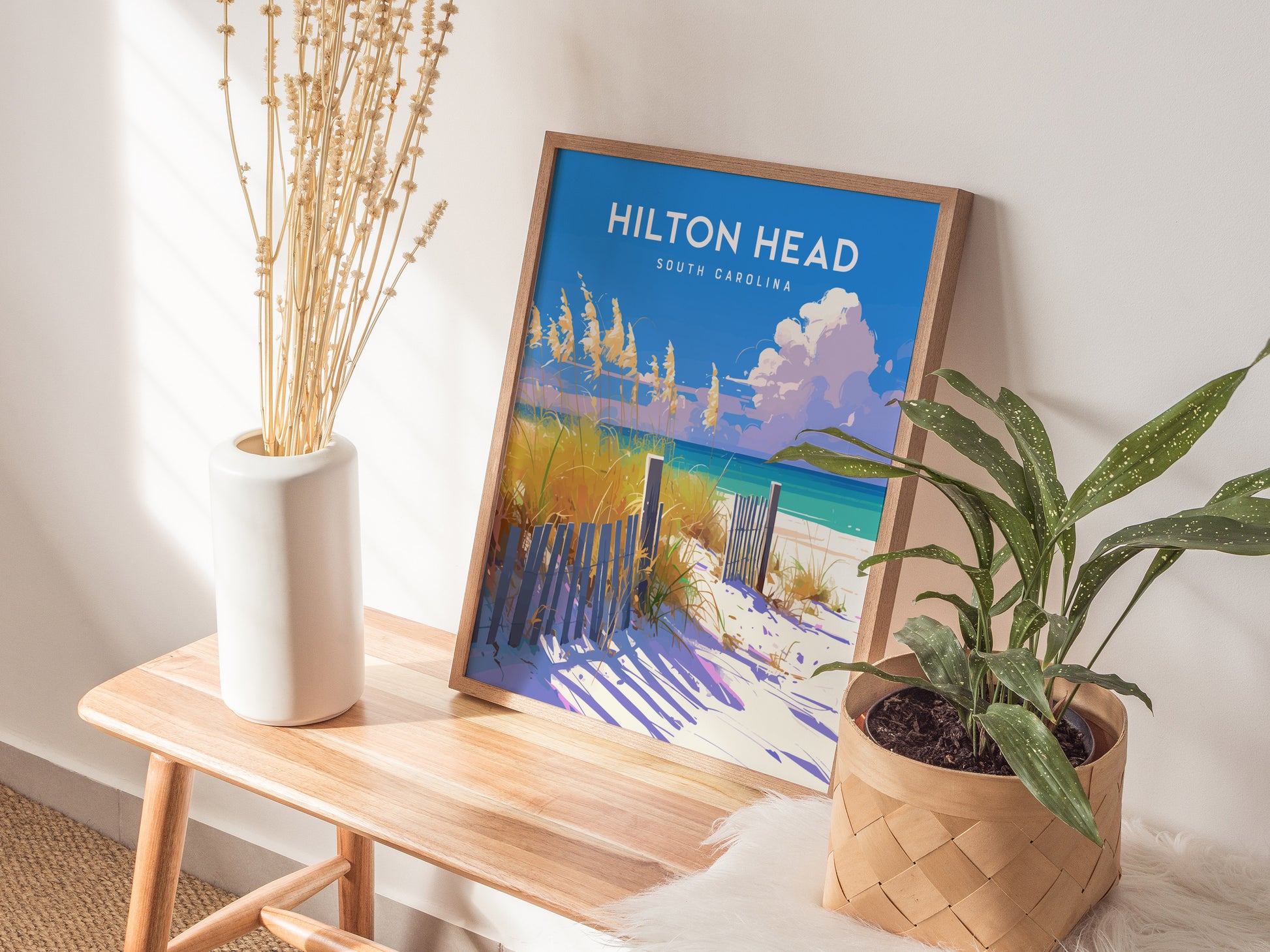 A framed poster of Hilton Head, South Carolina, featuring a beach scene with sand dunes and grasses, rests on a wooden bench.