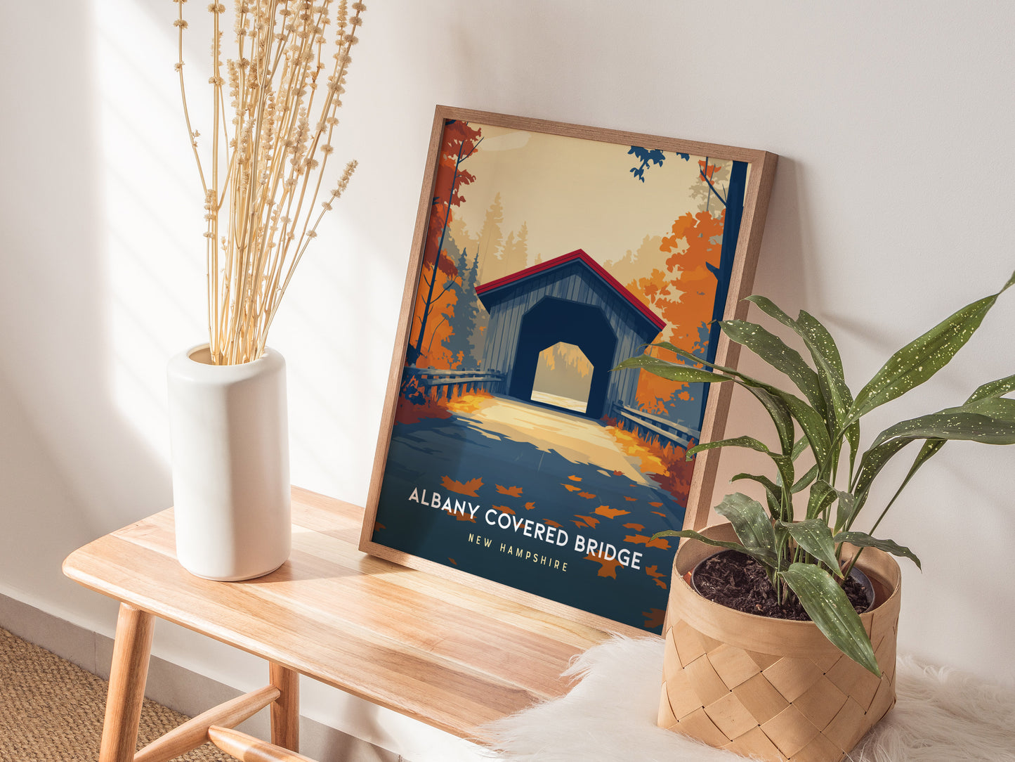 A framed poster of the Albany Covered Bridge in New Hampshire is displayed on a wooden table in a bright room.