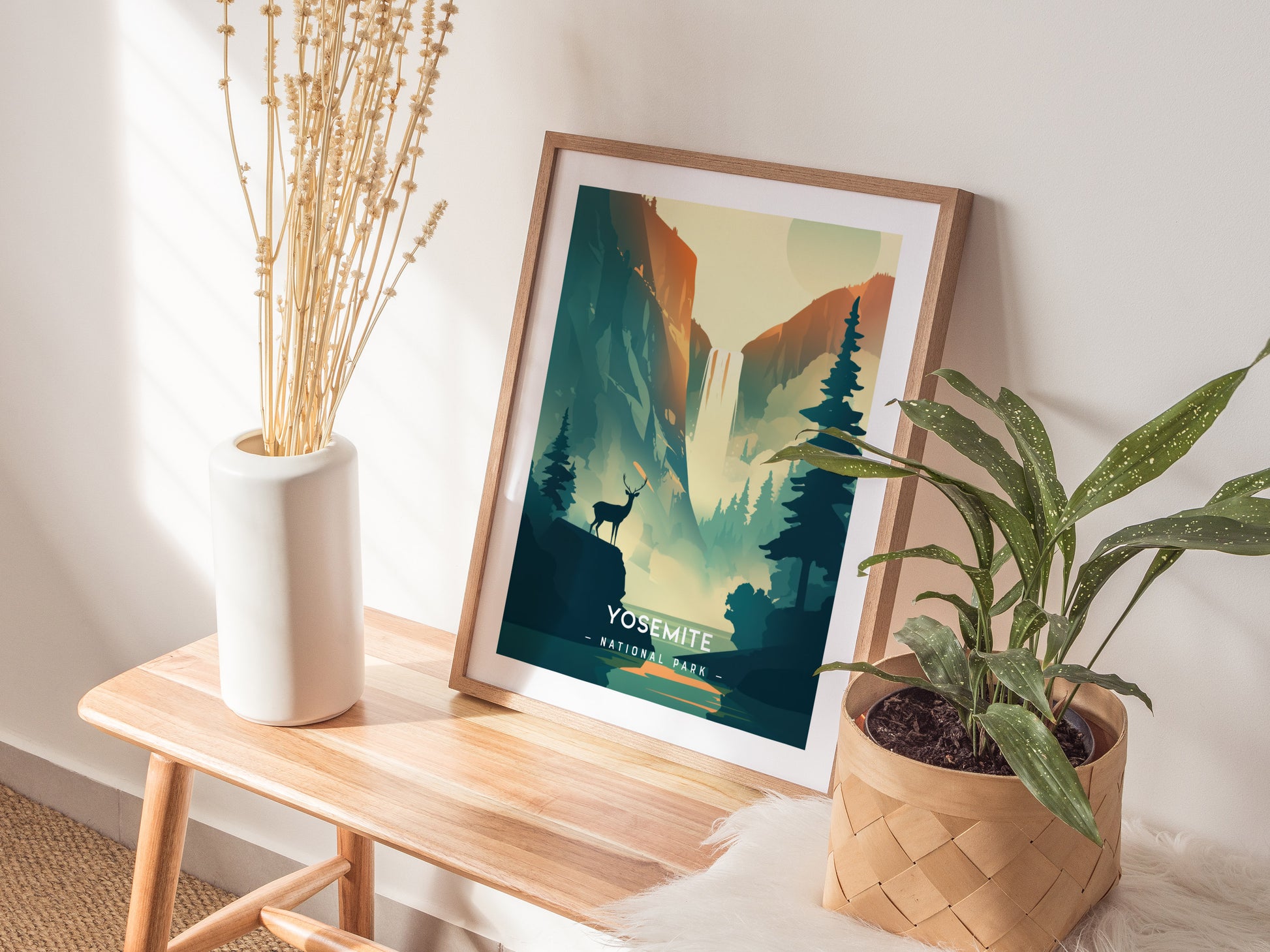 A framed Yosemite National Park poster with a minimalist design featuring a deer and pine trees is displayed on a wooden bench, alongside a white vase and a potted plant.