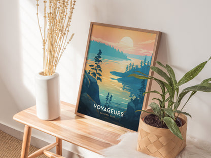 A framed Voyageurs National Park poster featuring a lake at sunset is displayed on a wooden bench, accompanied by a white vase with dried flowers and a potted green plant.