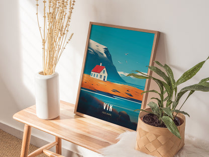 A wooden-framed poster depicting a coastal scene with a house is displayed on a bench, flanked by a white vase with dried stems and a green potted plant.