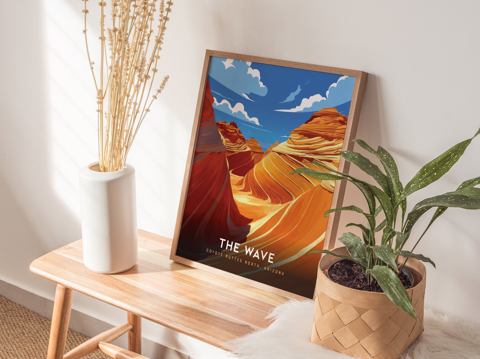 A framed poster of The Wave in Coyote Buttes, Arizona, rests on a wooden bench beside a white vase with dried stems and a potted plant.